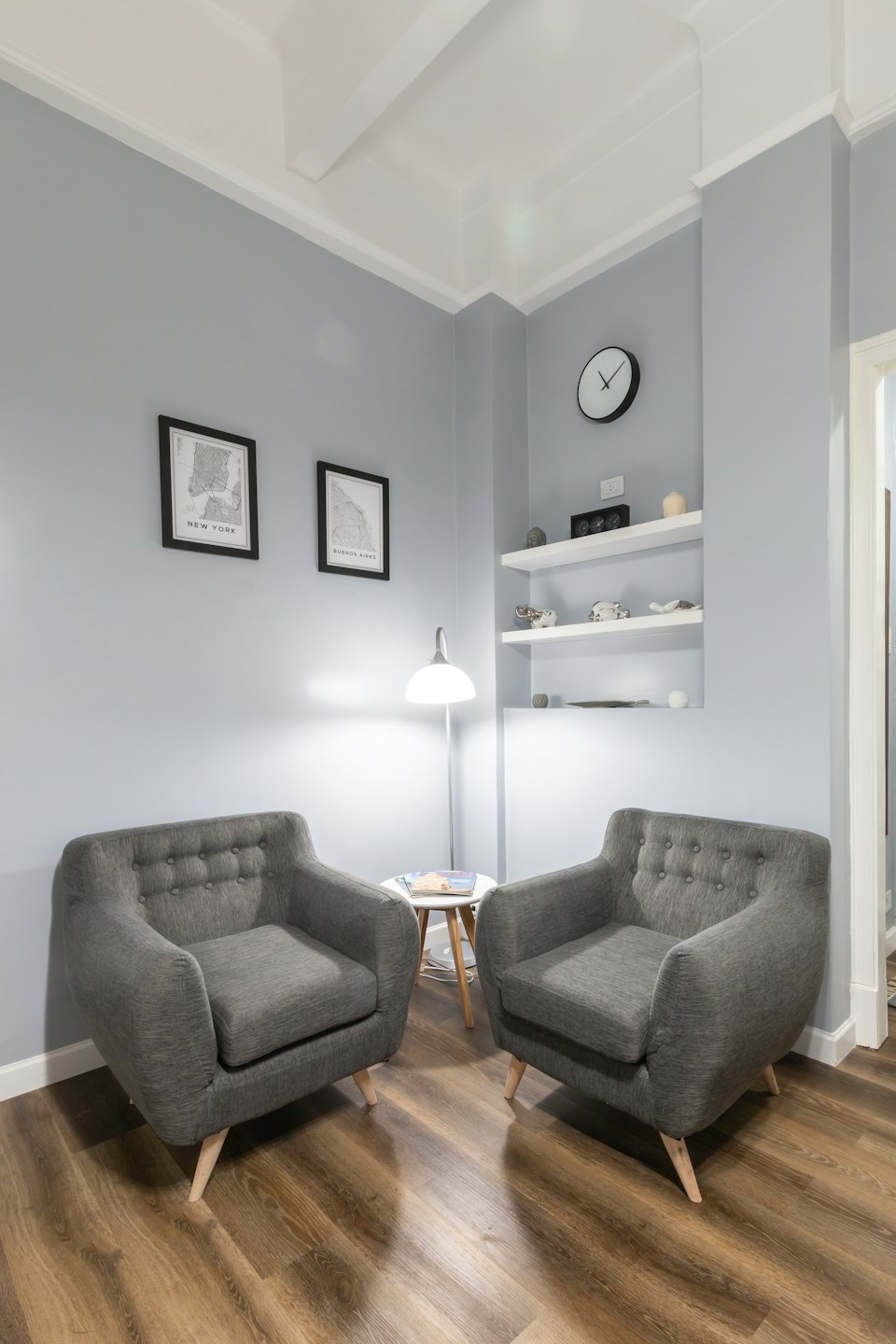 Two grey armchairs in a waiting area with map prints.