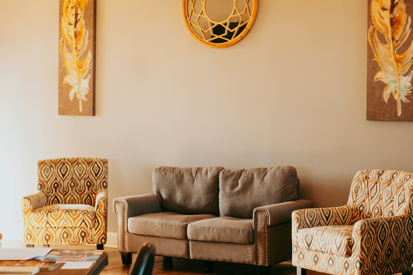 A sofa and two armchairs face a round wooden wall mirror.